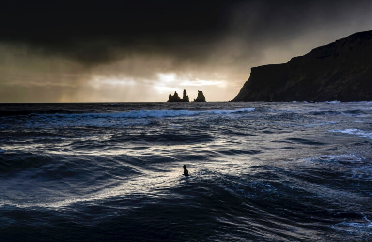 A dark scene with a large body of water and cliffs off in the distance.